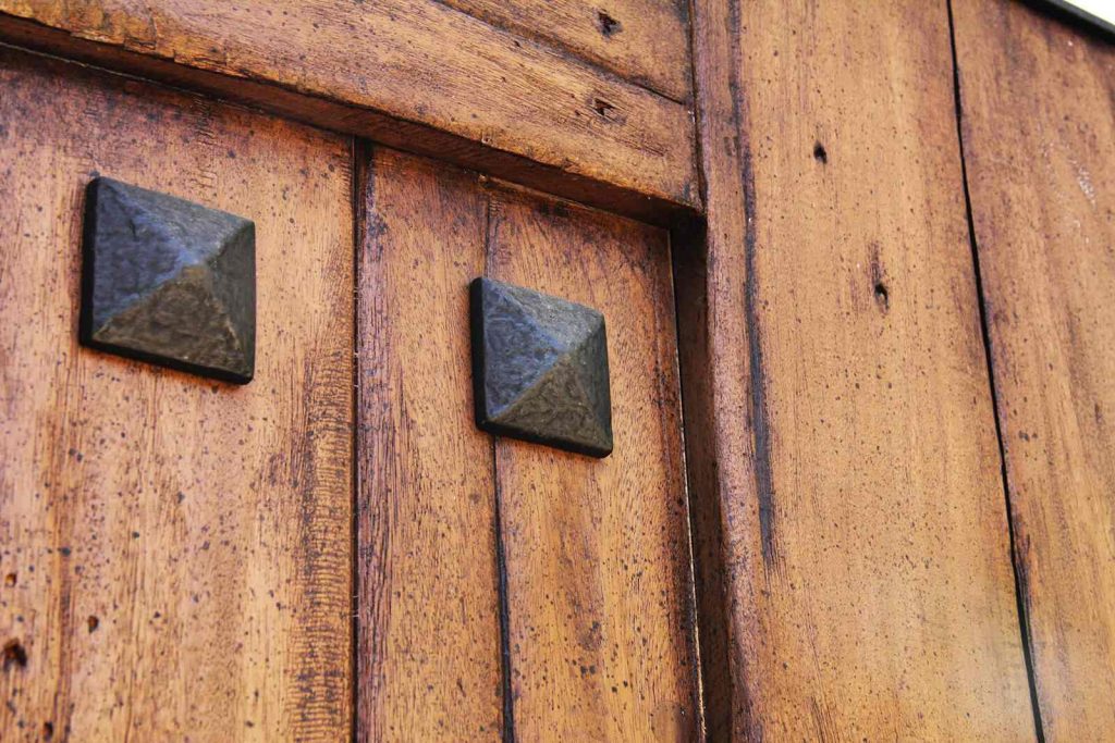 Close up of exotic hardwood gate with hand hammered cast iron door accents